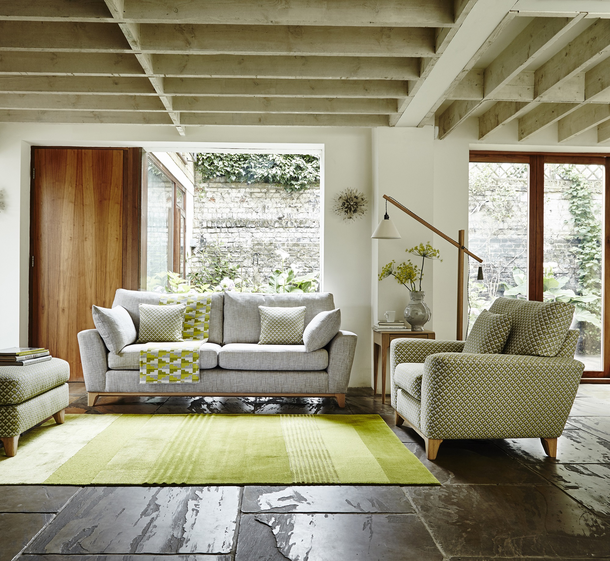 Ercol Grey Sofa with Yellow/Green Pillows and Throws and Green Accent Chair in a Bright Living Room with alot of Greenery 
