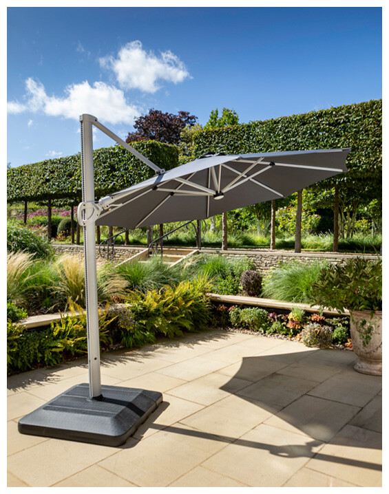 An image of a large parasol on a patio area surrounded by greenery.