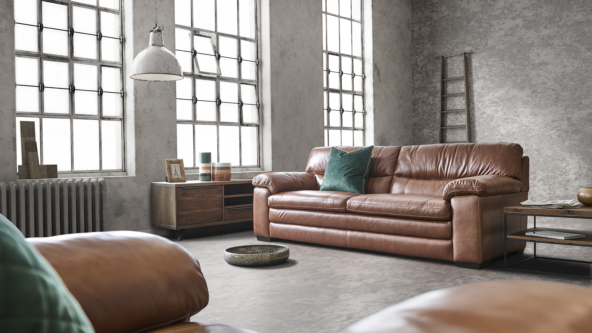 Industrial styled brown leather sofa sitting in a loft with grey walls and floor