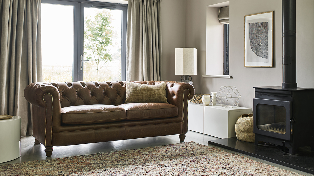 Brown chesterfield sofa in a living room with beige walls and a black fireplace