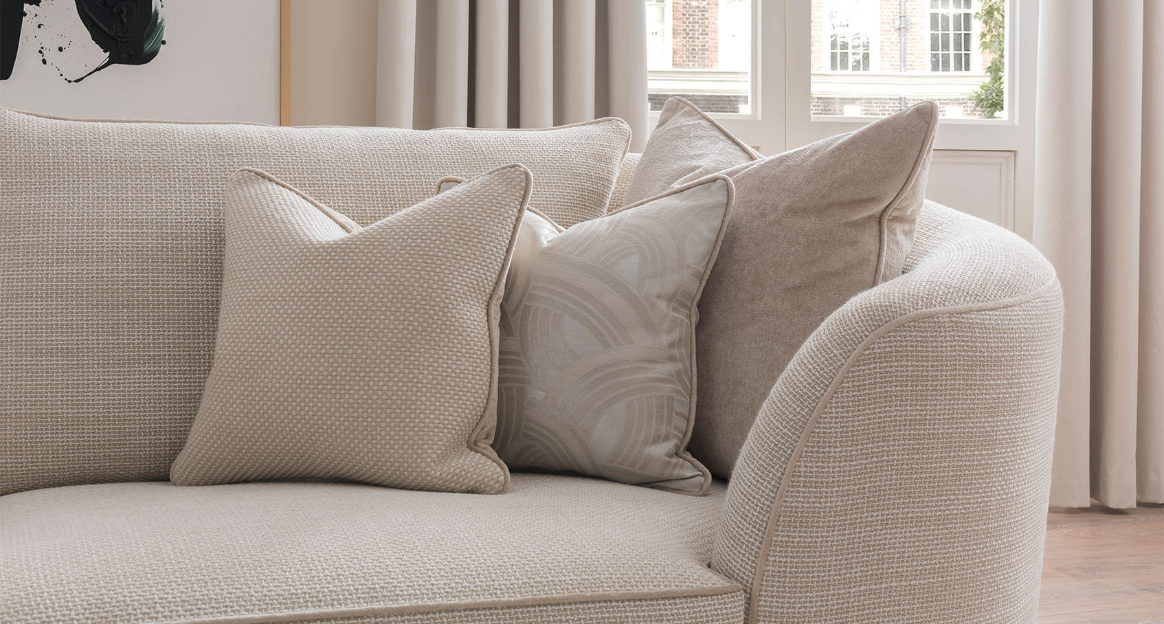 close up of the corner of a Duresta cream fabric sofa, styled with various cream toned cushions