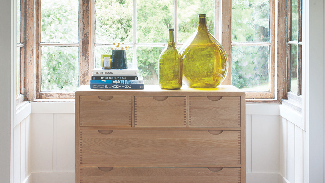 Ercol Bosco Bedroom Oak 5 Drawer Chest Displaying Two Large Vases In Front of a Big Window