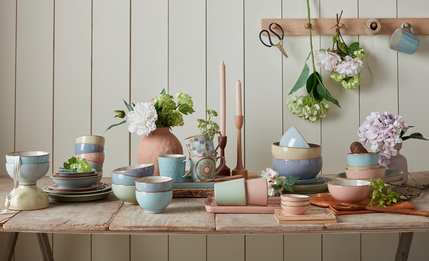 An image of pastel-coloured dinnerware scattered across a table with flower decorations.
