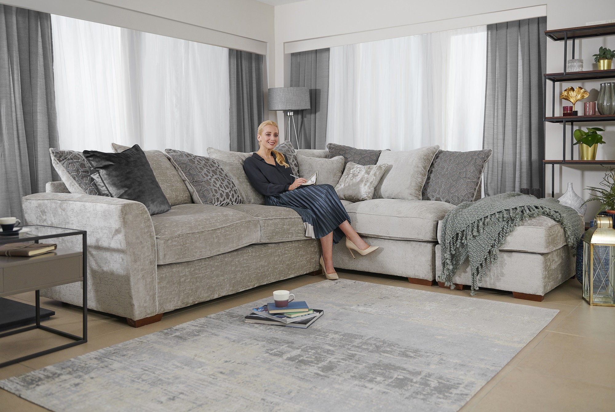 Grey velvet chaise sofa with a lady sitting on it with paper and pen in her hands in a stylish living room