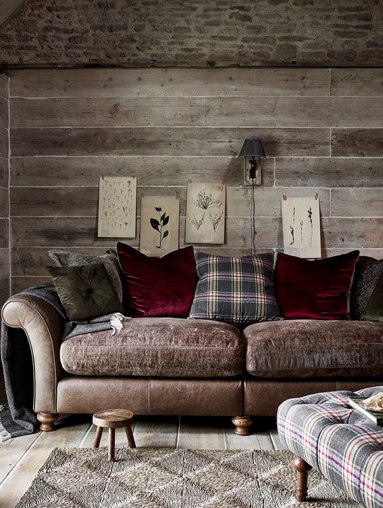 Cosy Alexander & James sofa made of leather and fabric with cushions and throw against a wooden wall in a country styled living room