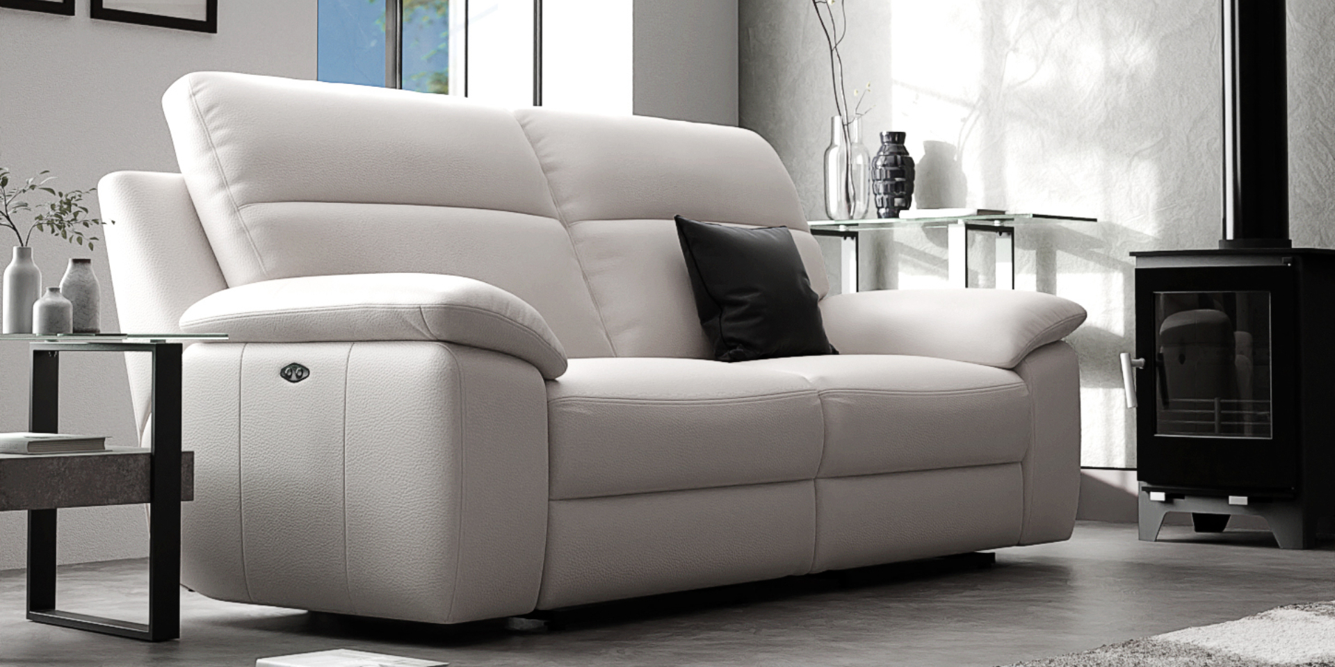 A white Italian leather sofa shown in a living room with grey walls with a black metal lamp table next to it and a black fireplace in the background