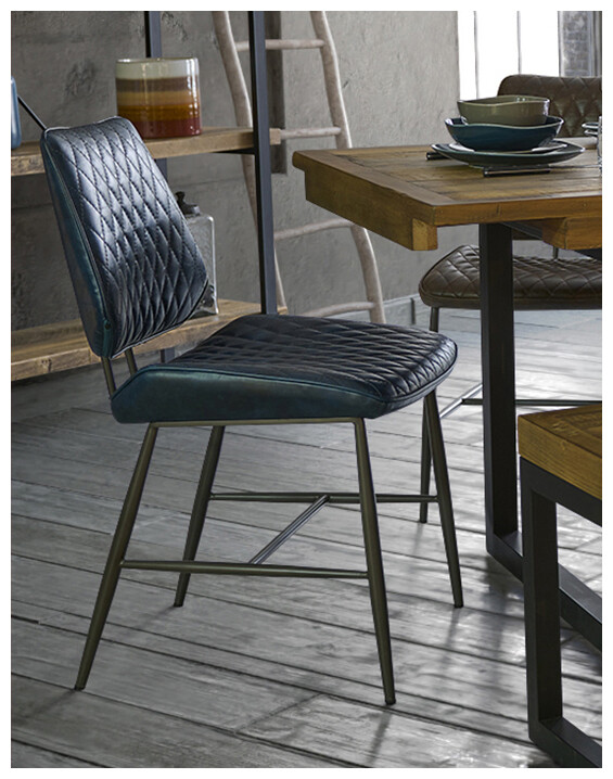 An image of the Starley Dining Chair in dark blue leather, set at a wooden table in a modern space.