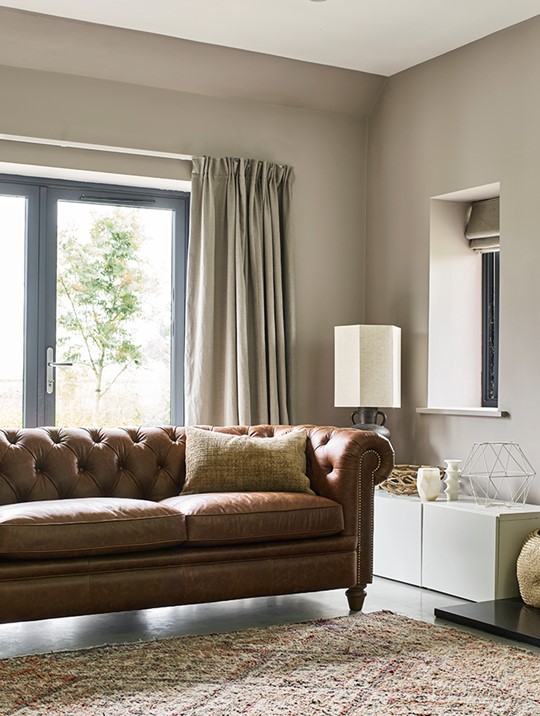 Brown leather A&J Stac chesterfield sofa in a neutral living room, next to a fireplace