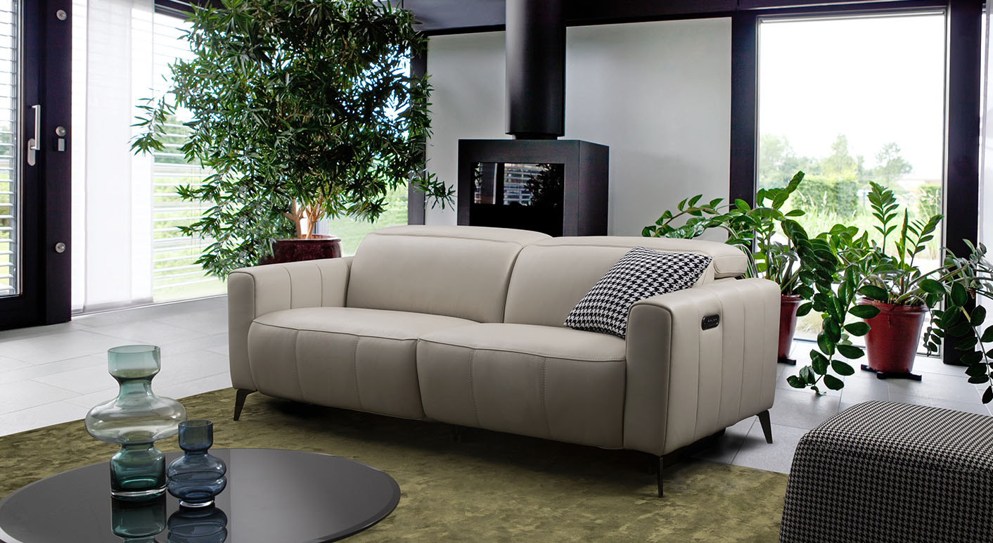 cream leather fabbrica 2 seater sofa in a light livingroom with greenery all around 