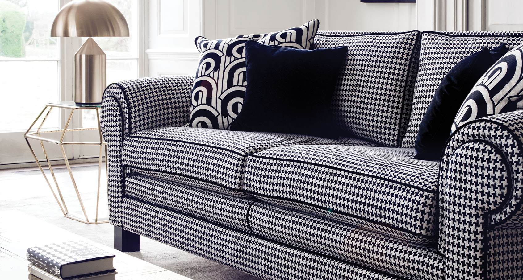 angled close up of coco two seater sofa in houndstooth pattern decorated with black and abstract cushions